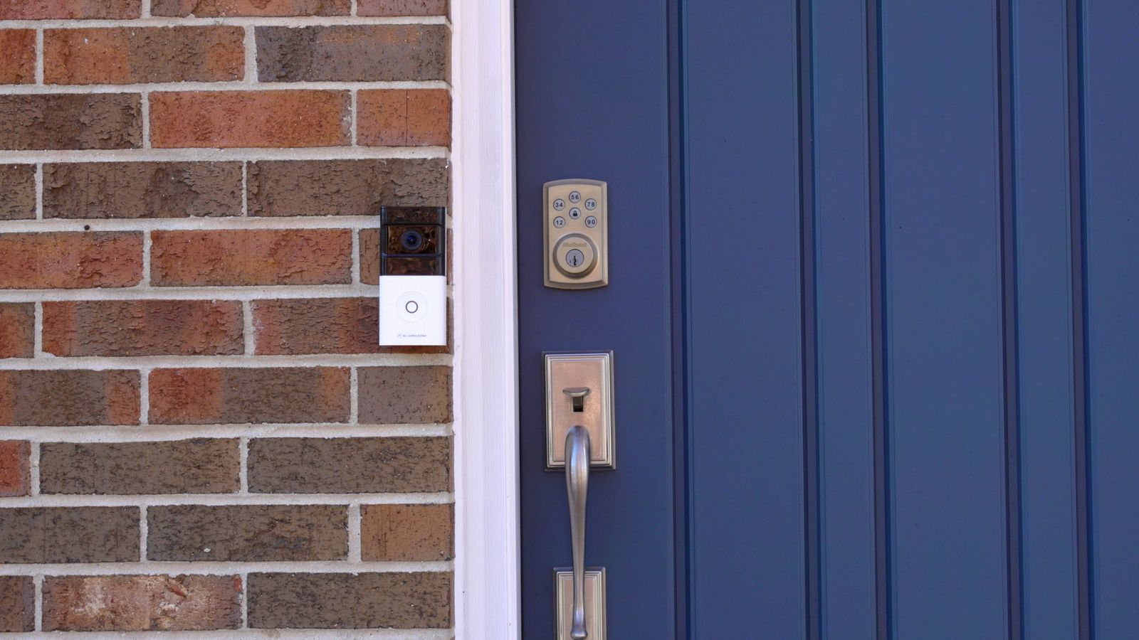 Alarm.com video doorbell mounted beside a blue front door on a brick house