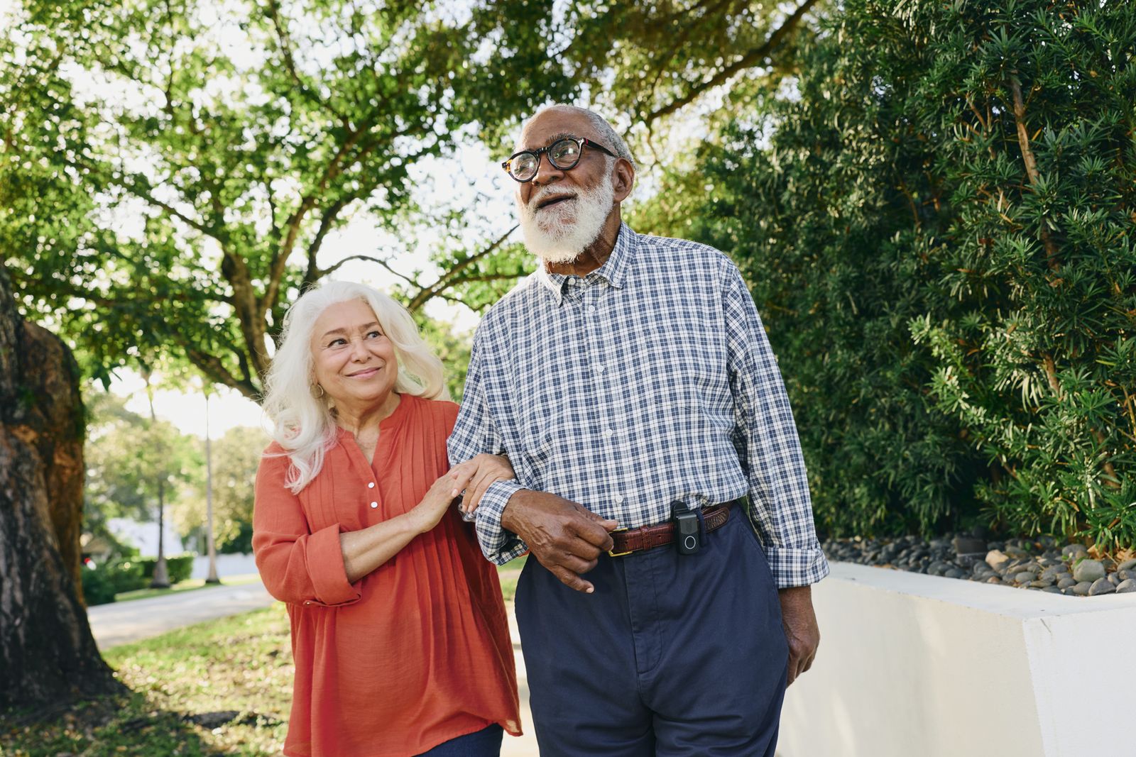 An older couple walking outdoors, the woman wearing an Indigo personal safety pendant