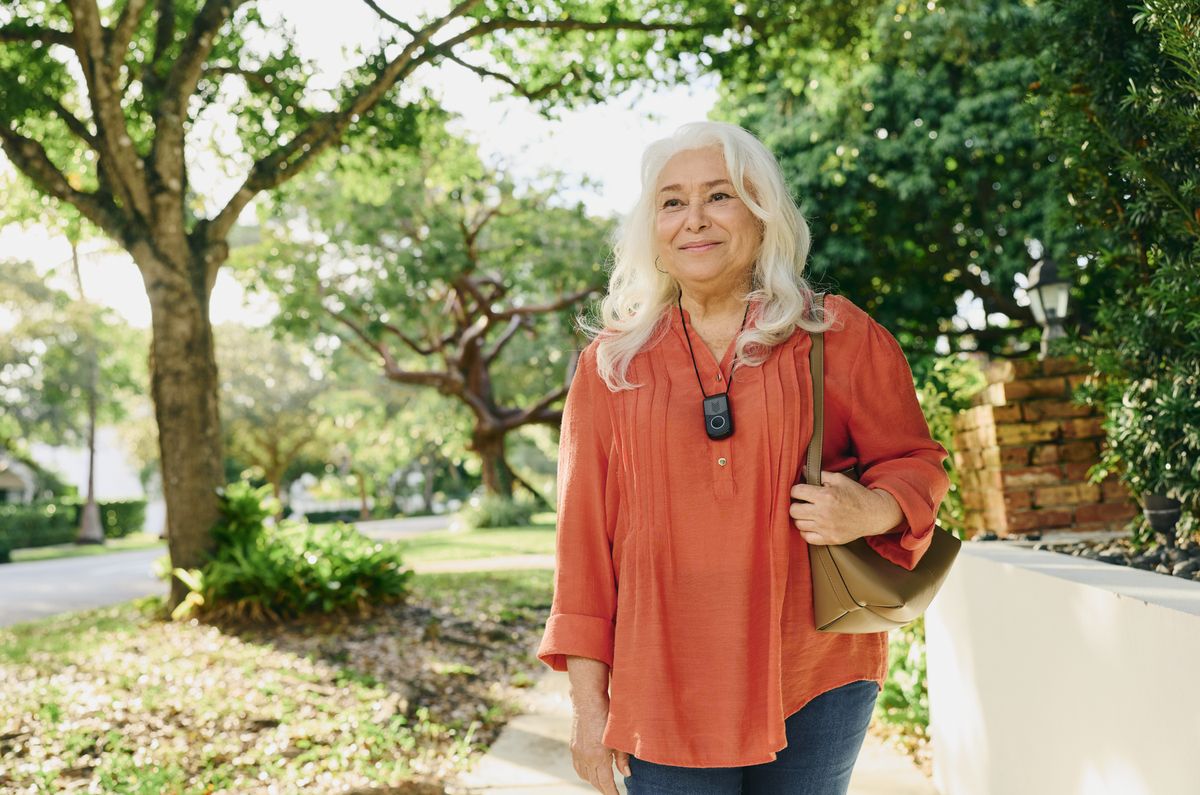 Older woman walking outdoors with an Indigo pendant on a lanyard